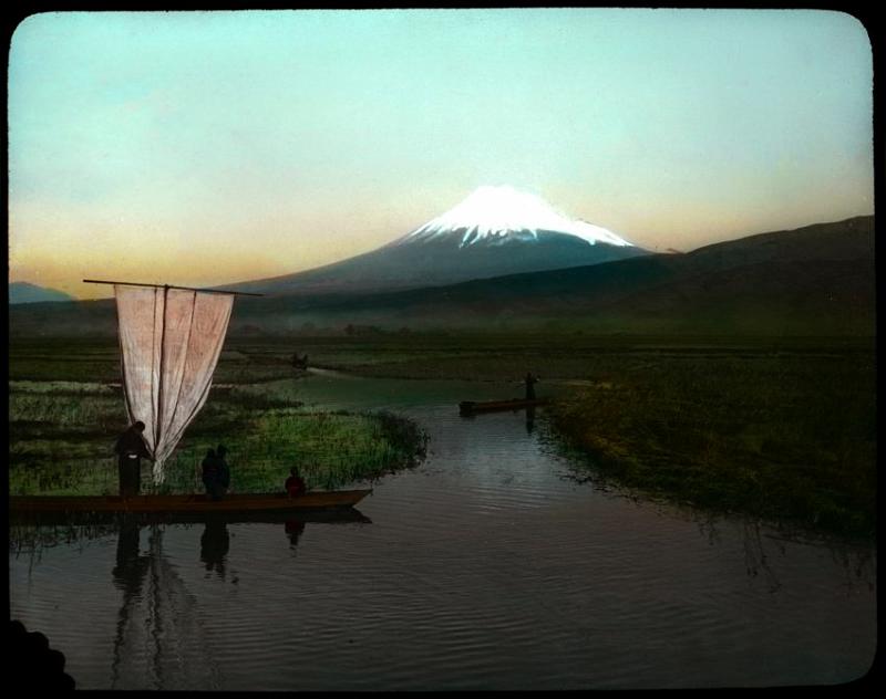 Fuji-05a-Geddes-1910.jpg - People travel in boats near the base of Mount Fuji. Item is a photographic glass-plate transparency; part of a set of colour-tinted transparencies depicting life in Japan ca. 1910, including scenery, street scenes, workers, farming, fishing, silk production, stone carvers, wood carvers, metal workers, potters, and artists. Photo by Herbert Geddes/University of Victoria Libraries